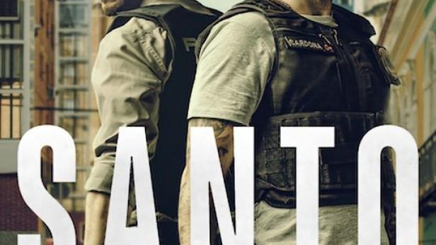 Zwei bewaffnete Männer stehen Rücken an Rücken vor einer Stadtkulisse.