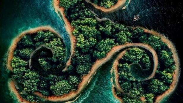 Eine Insel in Form eines Triskel-Symbols mit dichter Vegetation und zwei Booten im Wasser.
