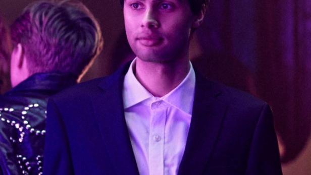 Ein Mann im Anzug steht in einer Bar und hält einen Cocktail.