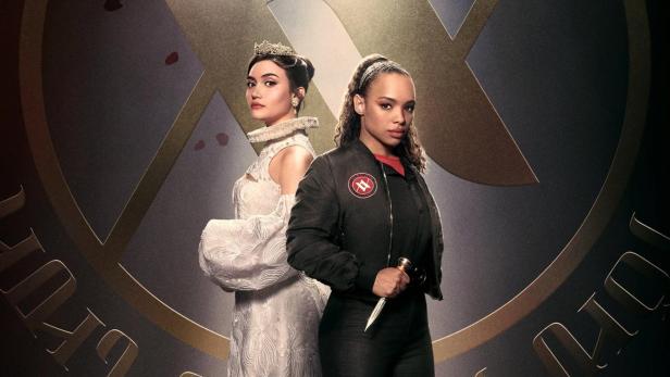 Zwei Frauen stehen vor einem Symbol für die „Vampire Academy“.