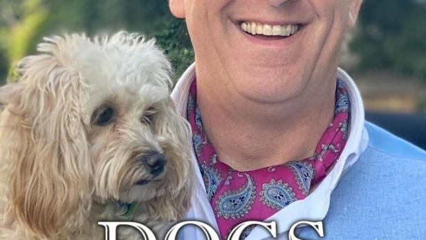 Ein Mann hält einen kleinen Hund im Arm und lächelt in die Kamera.