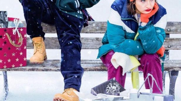 Ein Mann und eine Frau sitzen mit Einkaufstüten vor dem Eiffelturm im Schnee.