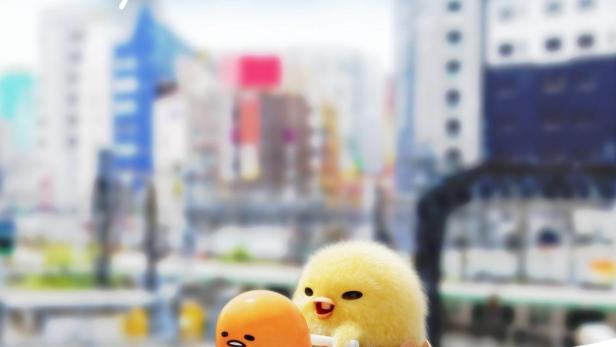Gudetama und ein Küken in Eierschalenwagen vor einer Stadtkulisse.