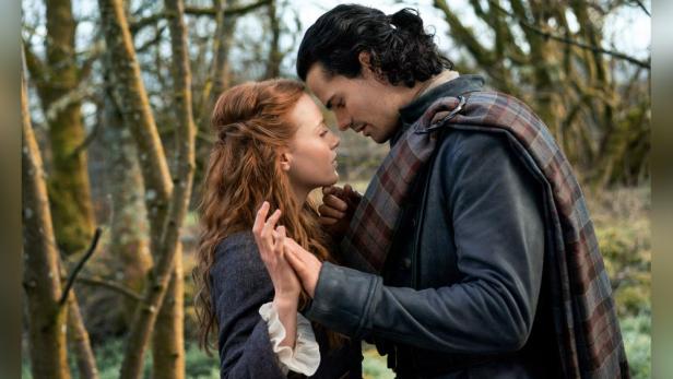 Ein Paar in historischer Kleidung steht eng umschlungen im Wald.