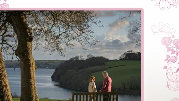 Ein Paar sitzt auf einer Bank mit Blick auf das Wasser, Titelbild für „Alte Herzen rosten nicht“ von Rosamunde Pilcher.