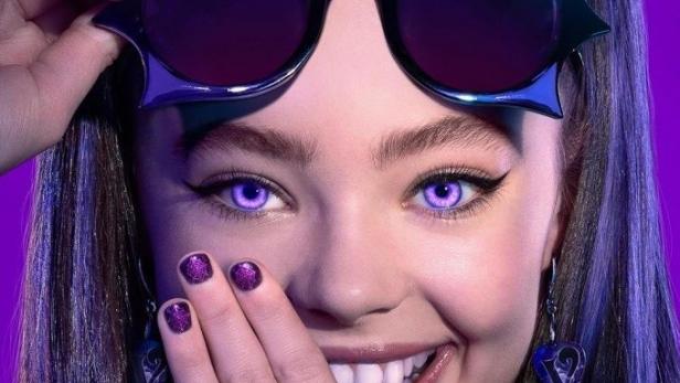 Ein junges Mädchen mit lila Augen und Vampirzähnen lächelt und trägt eine ausgefallene Sonnenbrille.