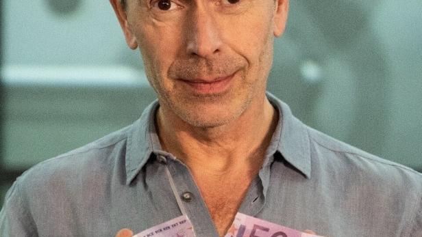 Ein Mann zerreißt zwei 500-Euro-Scheine vor einem Tresorraum, Titel: „Wem gehört die Welt? Eine Geschichte des Reichtums“.