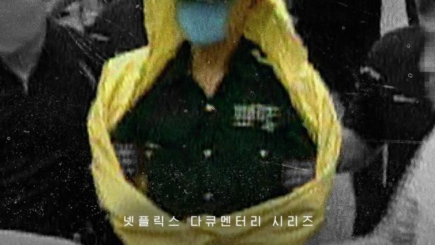 Ein Mann in Regenmantel und Maske inmitten einer Menschenmenge, vermutlich eine Szene aus der Netflix-Dokumentation „Raincoat Killer: Chasing Yoo Young-chul“.