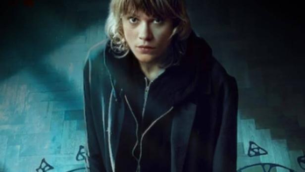 Eine junge Frau steht auf einem Boden mit okkulten Zeichnungen.