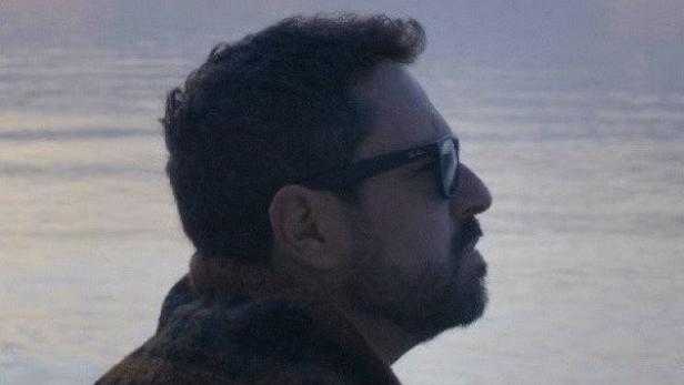 Ein Mann mit Sonnenbrille blickt auf das ruhige Wasser bei Dämmerung.