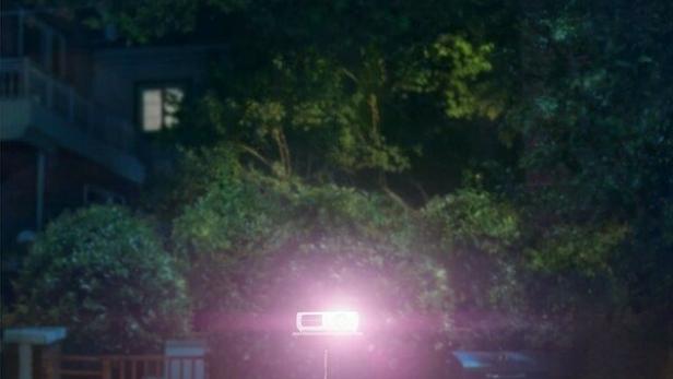 Vier junge Leute sitzen im Freien vor einer Leinwand und schauen einen Film.