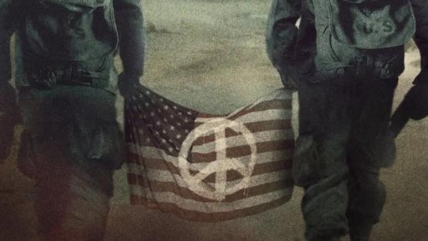 Zwei Soldaten tragen eine amerikanische Flagge mit einem Friedenssymbol vor einer Bergkulisse.