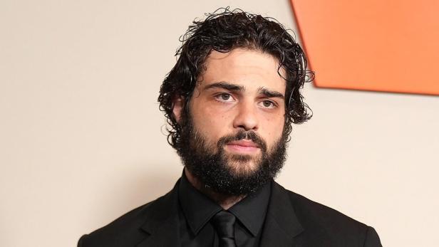 Porträt von Noah Centineo mit Bart und dunklem Anzug.
