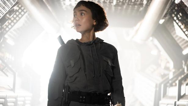 Eine junge Frau in einer futuristischen Umgebung blickt nach oben.