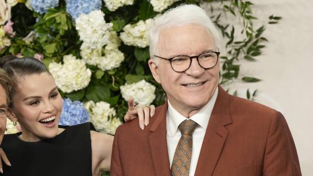 Steve Martin und Selena Gomez posieren vor einem Blumenhintergrund.