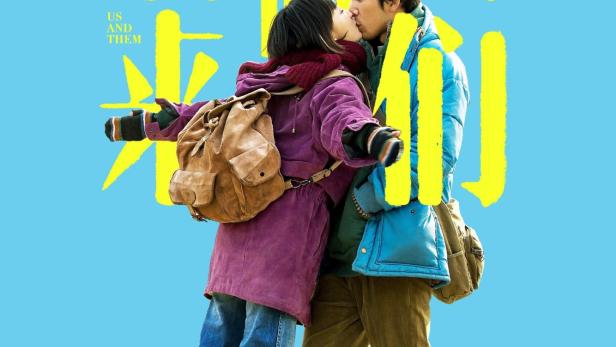 Ein Paar umarmt sich vor dem Hintergrund des Filmplakats „Us and Them“.