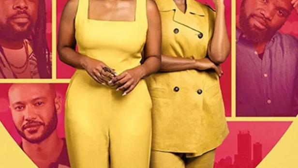 Zwei Frauen in gelber Kleidung stehen vor einem herzförmigen Hintergrund mit Porträts von Männern.