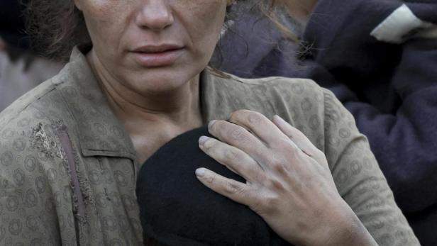 Eine besorgte Frau umarmt einen kleinen Jungen; andere Menschen stehen im Hintergrund.