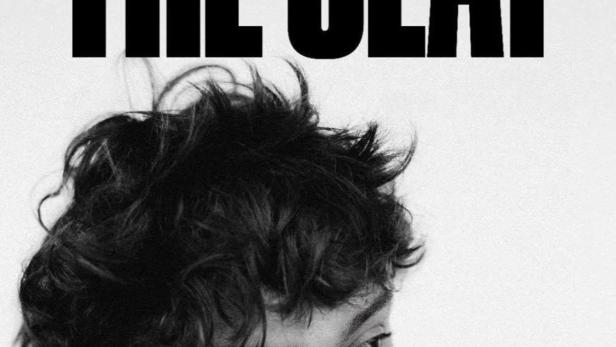 Ein junger Mann lächelt und hält seine Hände an die Wangen, über ihm der Titel „The Seat“.