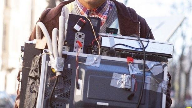 Julien Bam trägt eine mit Kabeln und Geräten verbundene Mikrowelle.
