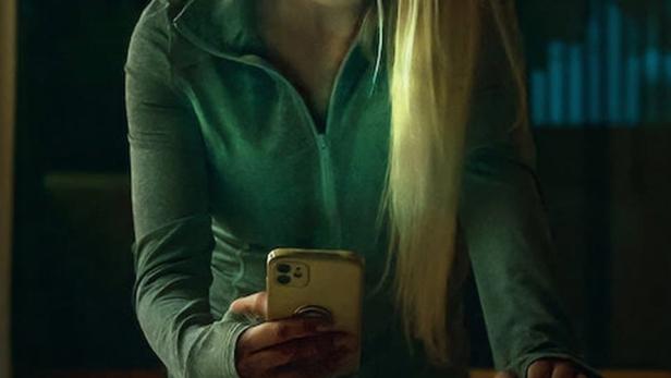 Eine junge Frau mit blonden Haaren schaut besorgt auf ihr Handy.