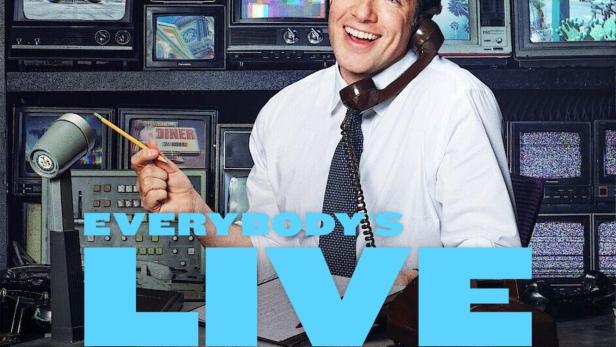 John Mulaney am Set von „Everybody's in LA“, umgeben von alten Fernsehern und Weltzeituhren.