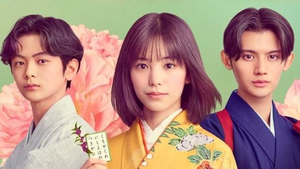 Drei junge Darsteller in traditioneller japanischer Kleidung vor einem floralen Hintergrund.