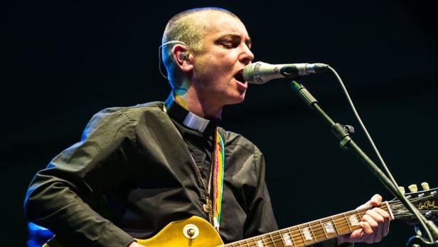 Sinéad O'Connor spielt Gitarre und singt in ein Mikrofon.