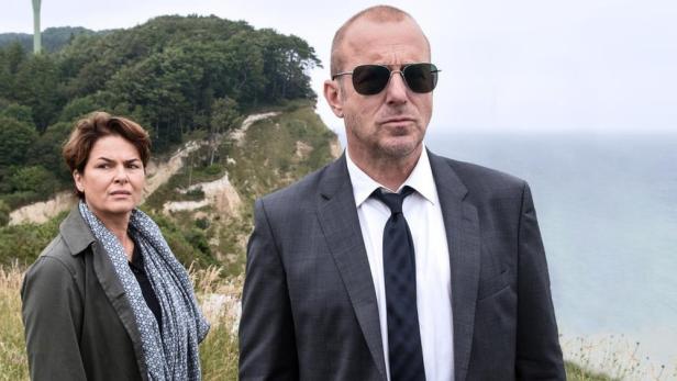 Ein Mann und eine Frau stehen vor der Küste auf einem Hügel, im Hintergrund der Titel „Die Verschwundene Familie“.