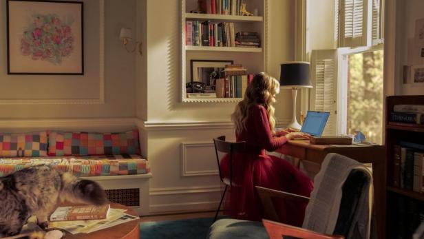 Eine Frau sitzt an einem Schreibtisch und arbeitet an einem Laptop in einem gemütlichen Zimmer.
