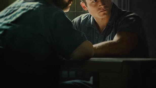 Zwei Männer sitzen an einem Tisch in dem Filmposter für „In With The Devil“.