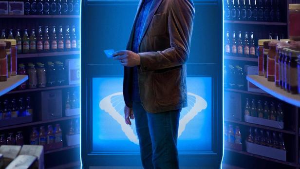 Ein Mann steht vor einer leuchtenden Maschine im Stil eines Verkaufsautomaten, Szene aus „The Big Door Prize“.