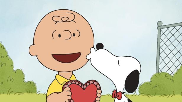 Charlie Brown hält ein Herz, während Snoopy ihn küsst.