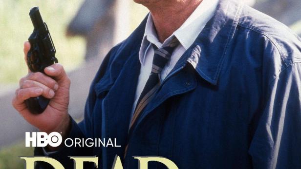 Ein Mann mit Kappe und Jacke hält eine Pistole in der Hand, im Hintergrund das Filmplakat „Dead Silence“.