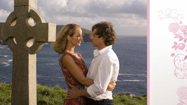 Ein Paar umarmt sich vor einem Steinkreuz und dem Meer, Titelbild von „Nebel über Schloss Kilrush“.