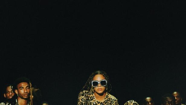 Beyoncé posiert mit anderen Darstellern für „Black Is King“ auf einem mit Leopardenmuster bedruckten Auto.