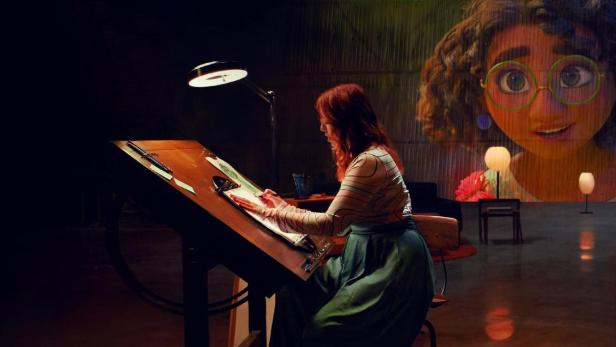 Eine Künstlerin zeichnet am Zeichentisch; im Hintergrund ist Mirabel Madrigal zu sehen.