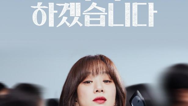 Eine Frau hält eine Sonnenbrille vor dem Hintergrund des Posters für eine koreanische Anwaltsserie.