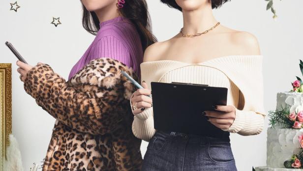 Zwei Frauen posieren vor dem Hintergrund des Schriftzugs „Planners“ und einer Hochzeitstorte.