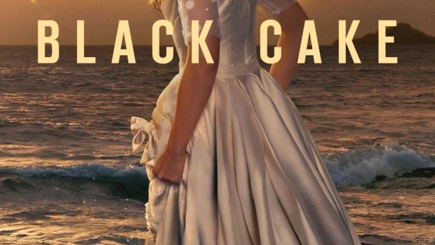 Eine Frau in einem hellen Kleid steht am Strand, im Hintergrund der Titel „Black Cake“.