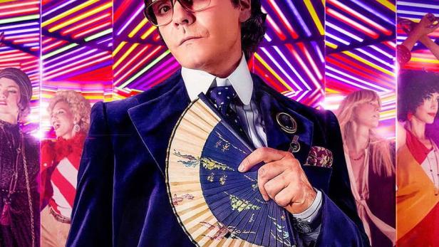 Ein Mann im blauen Samtanzug hält einen Fächer vor dem Hintergrund des Titels „Becoming Karl Lagerfeld“.