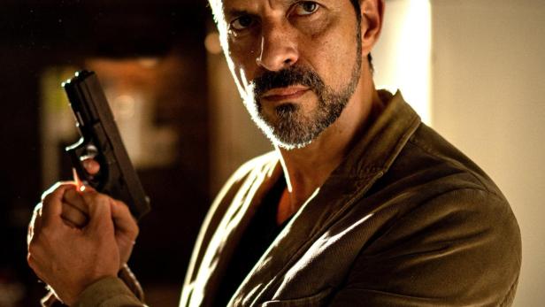 Ein Mann im braunen Jackett hält eine Pistole; Filmposter „Kommissar Dupin – Bretonische Nächte“.