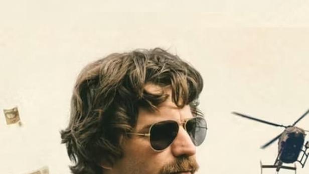 Ein Mann mit Sonnenbrille und Schnurrbart vor einem Hubschrauber, im Hintergrund der Titel „Ich bin Dagobert“.