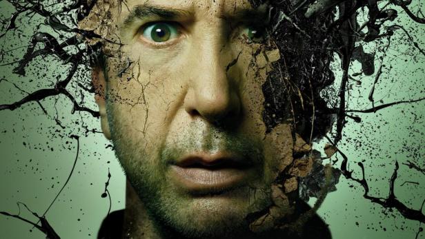 Ein Mann mit besorgtem Blick, dessen Gesicht teilweise von Rissen und schwarzer Farbe bedeckt ist, für „Gänsehaut: Die verschwundenen Kinder“.