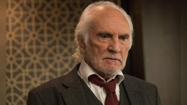 Porträt von Terence Stamp in einem dunklen Anzug und roter Krawatte.