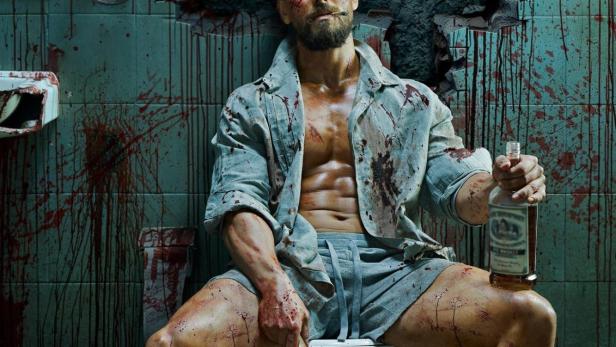 Ein blutverschmierter Mann sitzt mit einem Messer und einer Flasche auf einer Toilette; im Hintergrund der Titel „Baaghi 4“.