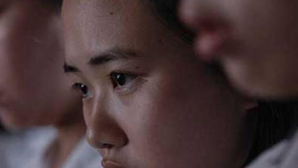 Eine junge Frau mit ernstem Blick in einem Klassenzimmer.