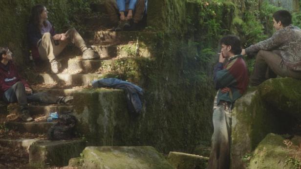 Eine Gruppe junger Leute sitzt und steht vor einem moosbewachsenen Gebäude.