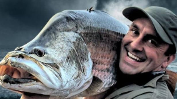 Ein Mann trägt einen riesigen Fisch vor dem Hintergrund des Titels „Chasing Monsters“.