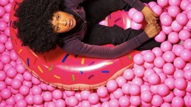 Eine Frau liegt auf einem Donut-förmigen Schwimmreifen in einem Becken voller pinkfarbener Bälle.